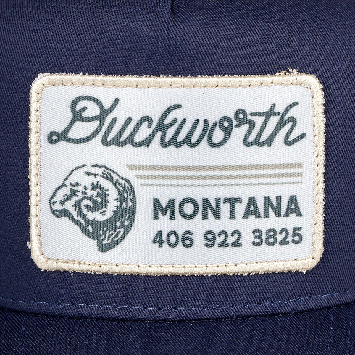 A Duckworth patch on a blue hat including a phone number and Ram head.
